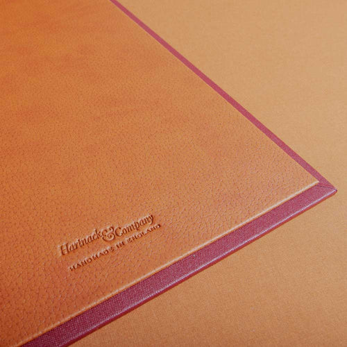 Close-up of a luxury leather-bound binder with 'Hartnack & Company' embossed on it, on a matching orange background.