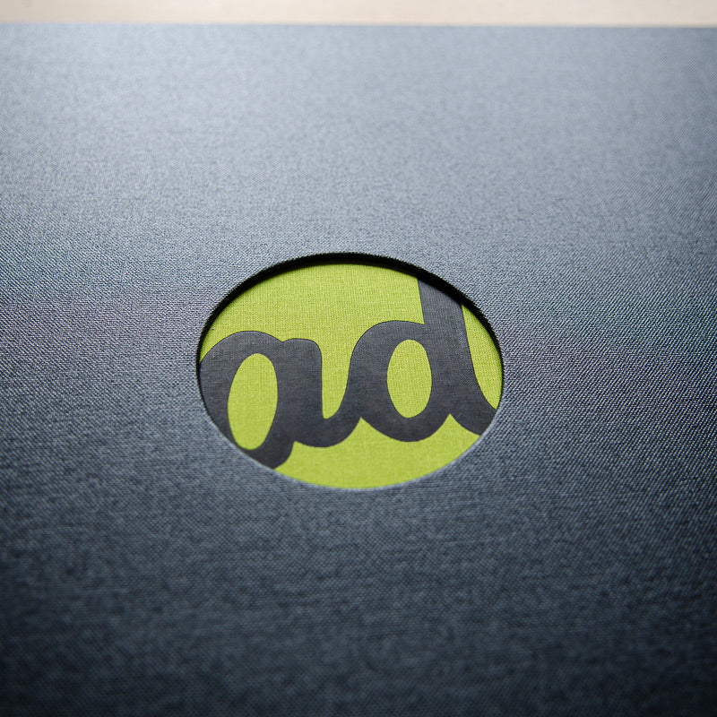 black foil logo on green fabric behind circular cut out for luxury design portfolio book - Gallery image 1