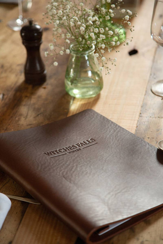 Rustic brown leather menu cover with embossed logo sitting on country pine table