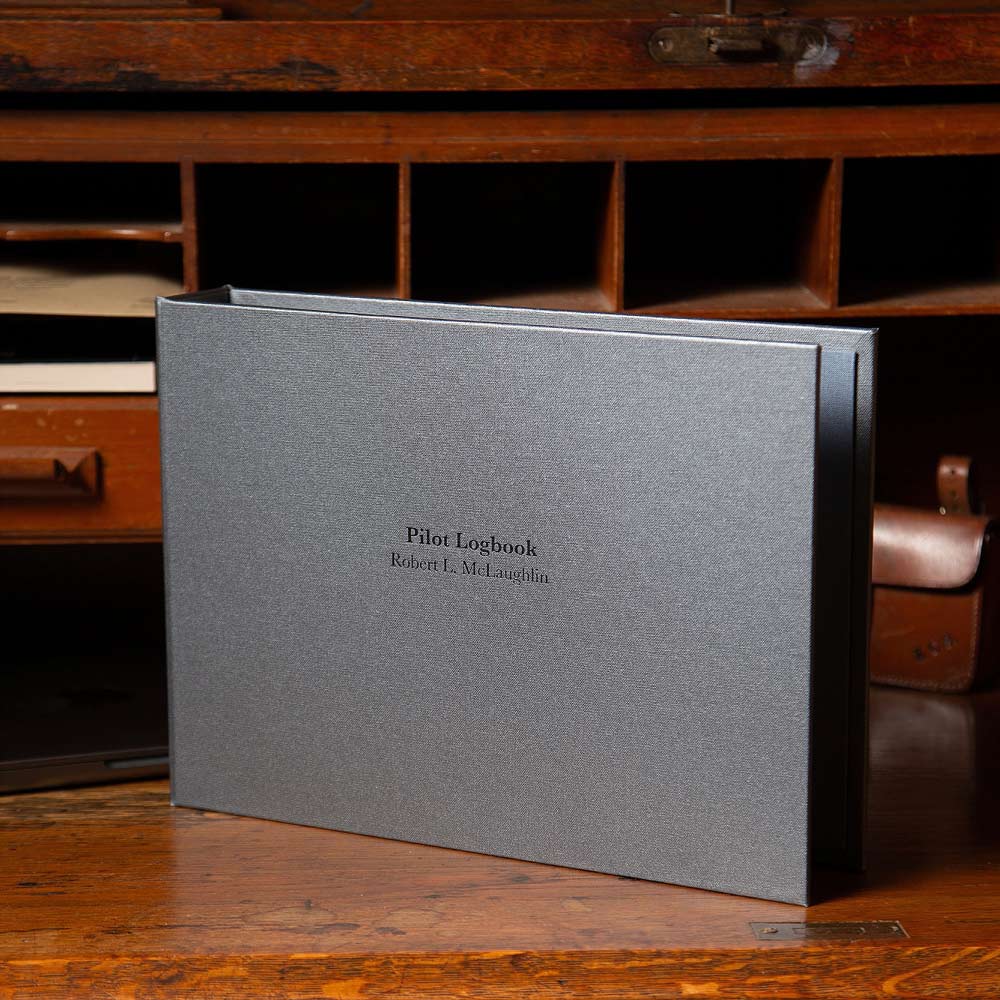 personalised pilot logbook binder in grey fabric with black printed name sitting on wooden furniture - Gallery image 1