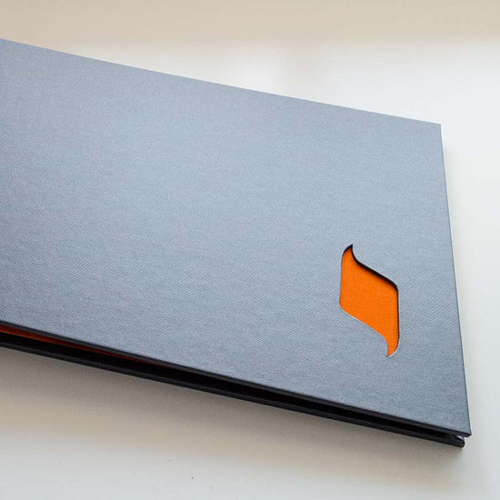 close up of a cut out logo shape in the grey cover of a portfolio book which has orange behind it