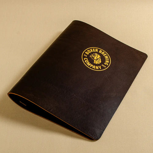A dark brown leather menu folder or binder with a gold circular logo for 'Boxer Brewing Company' gold foil embossed on the cover.