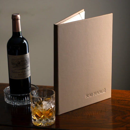 brown luxury leather menu cover with embossed cover sitting on wooden top next to wine bottle and whisky glass