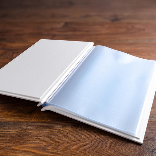 white screw post binder with plastic page pockets by hartnack and co on wood back drop