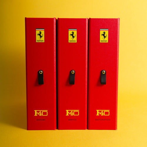 Three red Ferrari F40 history box files with yellow and black printed details of the car and logos on a yellow background