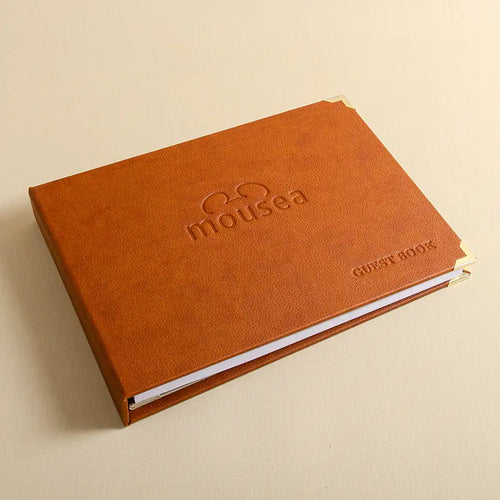 A tan brown textured faux leatherette guest book with the logo blind embossed on the front cover, with brass corner protectors all resulting in a very high class top quality product