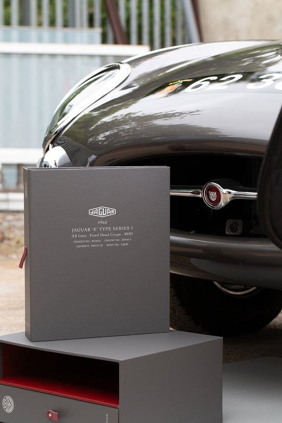 ring binder history file in grey book cloth and red lining sitting in front of an etype Jaguar