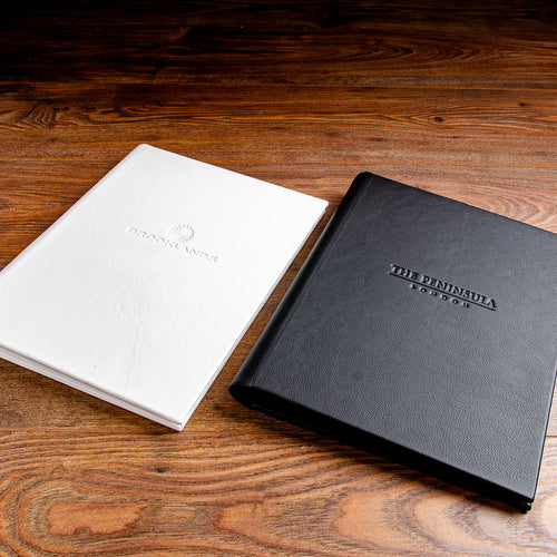 Black and white leather menus with embossed covers sitting on a wooden back ground