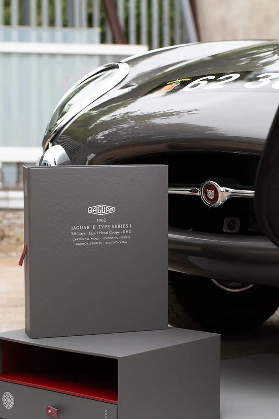 ring binder history file in grey book cloth and red lining sitting in front of an etype Jaguar