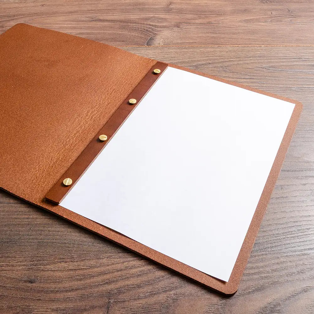 Brown leather menu cover with screw posts and a white page on a wooden surface