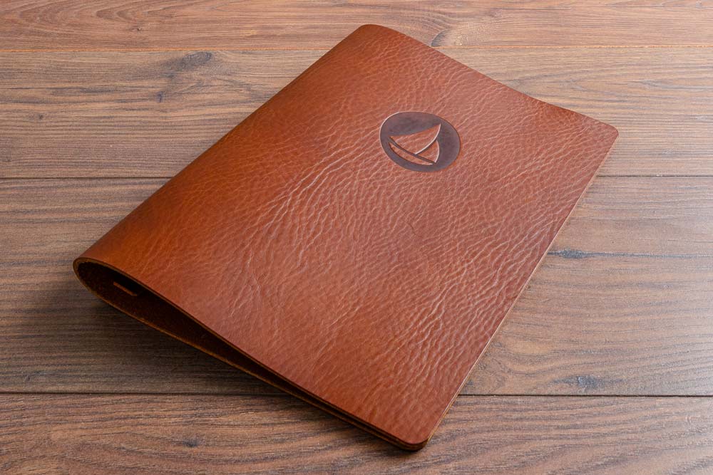Brown saddle hide leather menu cover with a personalised embossed logo on a wooden surface - Gallery image 1