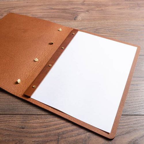 Brown leather menu cover with screw posts and a white page on a wooden surface