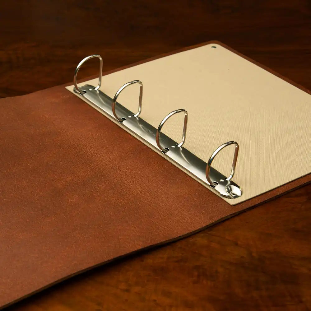 Brown Leather Ring Binder in high quality veg tan leather with 4-ring chrome mechanism on wood table surface.