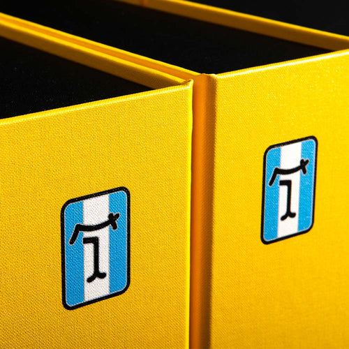 Close-up of a yellow box with blue and white De Tomaso logos UV printed on the spine.