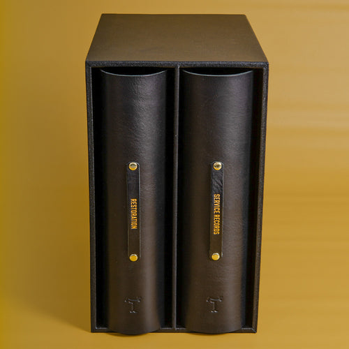 Black leather binders in a slipcase for a classic car service history and restoration on a yellow back ground