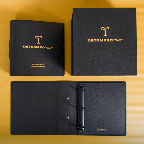 A set of black binders and a box with gold Detomaso logo and car details embossed on the cover for car history files