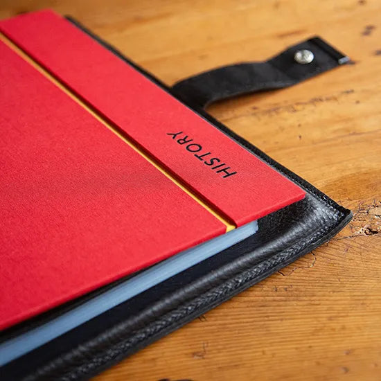 corner section of a custom made ring binder in red book cloth in a black leather holder with black embossed lettering