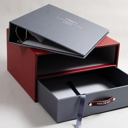 A luxury leather bound box with a pull out drawer with red leather embossed handles and silver grey ring binder with silver embossed cover for Aston Martin DB5 car history and documents