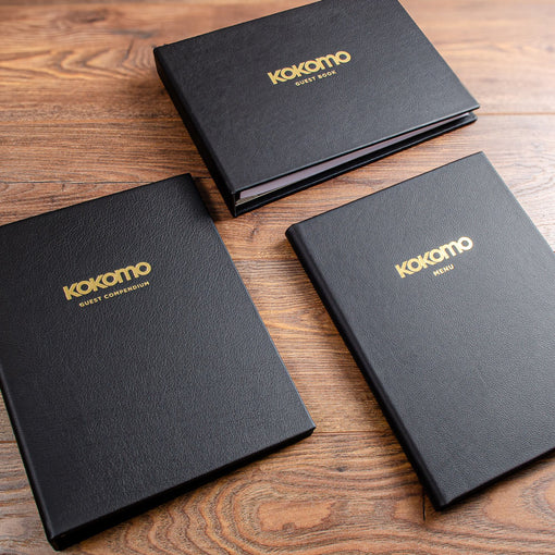 A collection of three black leather binders with the logos of a yacht gold foiled onto the covers and then the titles of; guest compendium, guest book and menu also gold foiled onto the cover 