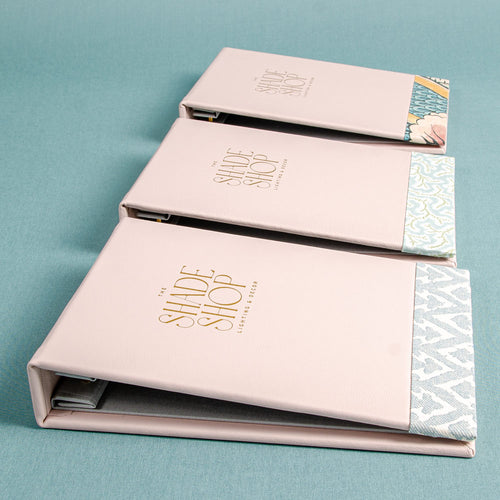 Three leather screw post binders for swatch books with Shade Shop logo foil embossed on the cover and fabric detail on he bottom of the cover