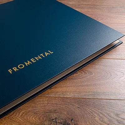 Blue fabric swatch book binder on wooden floor with gold foil logo embossed on the cover