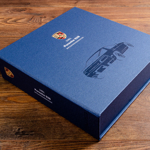 Blue Porsche car history document box with 928 illustration on the cover sitting a wooden surface