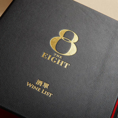 A close-up of a black textured leather wine list cover with gold foil lettering that reads 'THE EIGHT' and 'WINE LIST'.