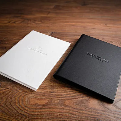 Black and white leather menus with embossed covers sitting on a wooden back ground