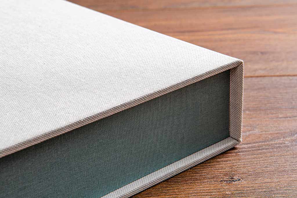 The inner tray on this clamshell box is covered in Pampas Green Windsor book cloth and the outer cover is in a Medium Linen book cloth. While beautiful, book cloth is not water resistant so we recommend buckram as an outer cover 